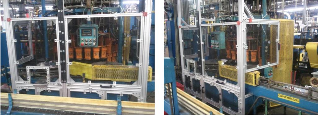 Automated manufacturing equipment enclosed with aluminum frame safety guards and mesh panels around robotic and mechanical components in a factory setting.