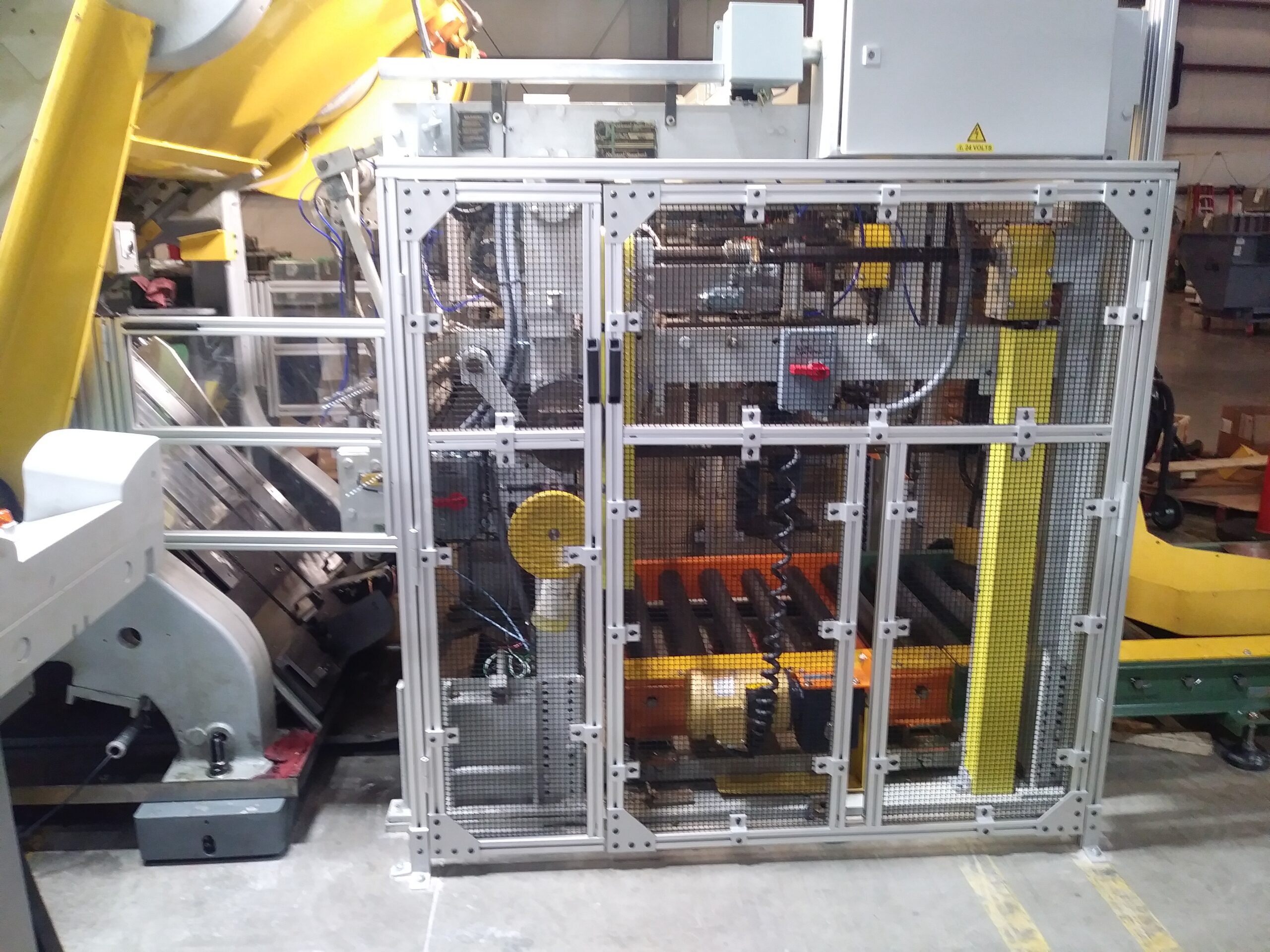 Machine guarding safety cage with wire mesh panels, aluminum extrusion frame, and an external control box featuring a blue reset light and emergency disconnect.